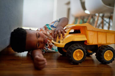 Cute boy playing with dump truck on hardwood floor at home - CAIF33580