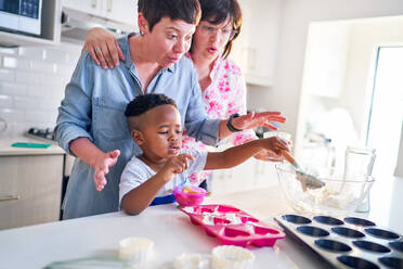 Lesbian couple and cute son baking heart-shape cupcakes in kitchen - CAIF33583