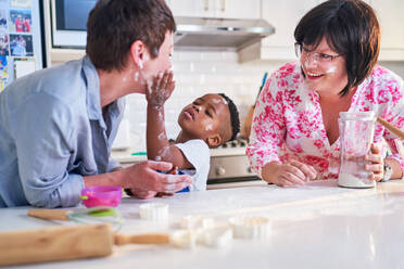 Playful, messy lesbian couple and son baking in kitchen at home - CAIF33585