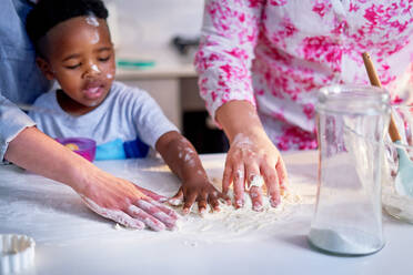 Lesbian couple and son baking, spreading flour on kitchen counter - CAIF33586