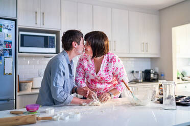 Affectionate lesbian couple baking, kissing in kitchen at home - CAIF33587