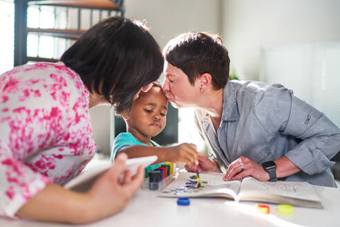 Affectionate lesbian couple kissing cute son painting at home - CAIF33590