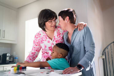 Happy, affectionate lesbian couple with son painting at home - CAIF33594