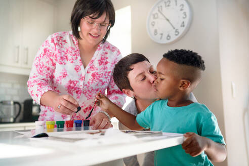 Affectionate lesbian couple kissing son painting in coloring book - CAIF33596