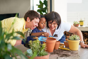 Happy lesbian couple and son planting plants in flowerpots on patio - CAIF33600