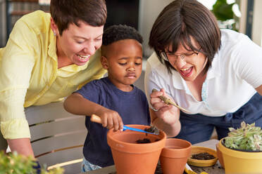 Happy lesbian couple watching son planting plants in flowerpots - CAIF33601