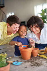 Happy lesbian couple watching son planting in flowerpots - CAIF33602