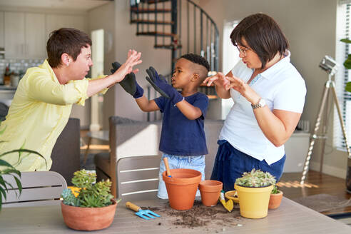 Playful lesbian couple and son gesturing, planting plants on patio - CAIF33636