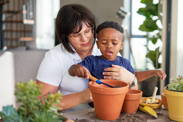 Mother and son planting plants in flowerpots on patio - CAIF33638