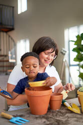 Mother and son planting in flowerpots at home - CAIF33639