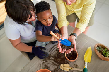 Lesbian couple and son digging in dirt, planting in flowerpots - CAIF33642