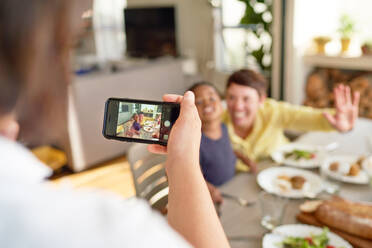 Woman with camera phone photographing wife and son at dinner table - CAIF33645