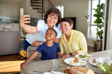 Ein freudiger Familienmoment: Ein lesbisches Paar und sein Sohn machen ein Selfie am Esstisch - CAIF33647