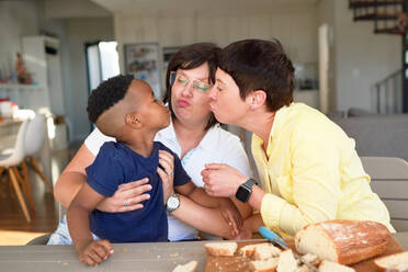 Lesbian couple and cute son puckering lips at dinner table - CAIF33651