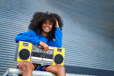 Portrait happy, cool young woman with boom box in alley - CAIF33654