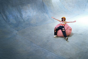 Portrait carefree young woman in beanbag chair on skate ramp - CAIF33659
