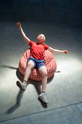 Portrait carefree young man falling back on bean bag chair - CAIF33663