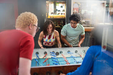 Happy young friends playing foosball in game room - CAIF33676