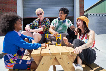 Happy young friends laughing, listening to music with boom box - CAIF33679