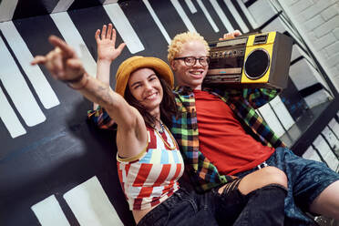 Portrait playful young friends listening to music with boom box - CAIF33691