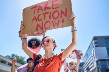 Young female protester holding action sign overhead in sunny city - CAIF33709