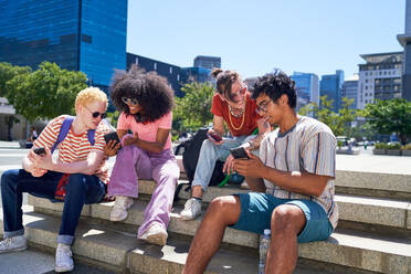 Young friends hanging out, using smart phones in sunny city park - CAIF33710