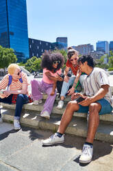 Young friends hanging out, using smart phones in sunny city park - CAIF33711