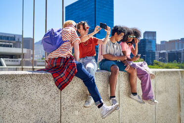 Young friends hanging out, using smart phones in sunny city - CAIF33718