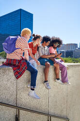 Young friends hanging out on ledge in sunny city - CAIF33719