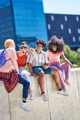 Young friends laughing, hanging out on ledge in sunny city - CAIF33723