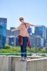 Portrait cool young man standing on ledge in sunny city - CAIF33727