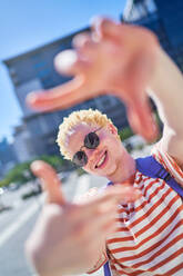 Portrait happy young man gesturing finger frame in sunny city - CAIF33736