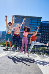 Portrait happy young friends jumping for joy in sunny city - CAIF33737