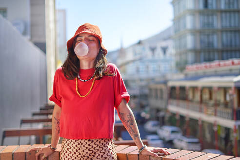 Portrait young woman blowing bubble gum bubble on rooftop - CAIF33745