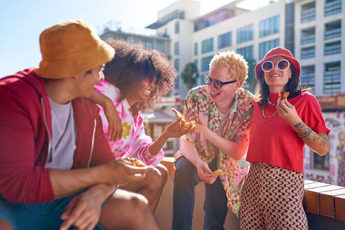 Happy young friends eating pizza, hanging out on sunny city rooftop - CAIF33750