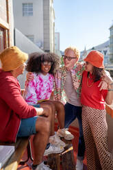Happy young friends hanging out, talking on sunny city rooftop - CAIF33752