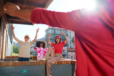 Happy young friends cheering on sunny, urban apartment balcony - CAIF33757