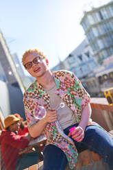 Portrait young man blowing bubbles on sunny urban balcony - CAIF33767