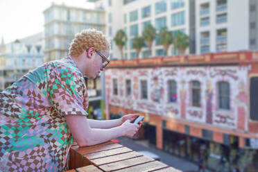 Young man using smart phone on urban balcony - CAIF33775