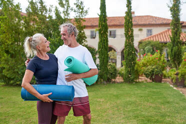 Happy senior couple with yoga mats in villa garden - CAIF33789