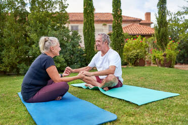 Happy senior couple holding hands on yoga mats in villa garden - CAIF33793