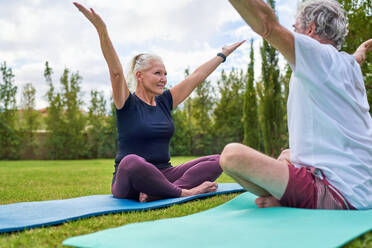 Happy senior couple practicing yoga together in park grass - CAIF33794
