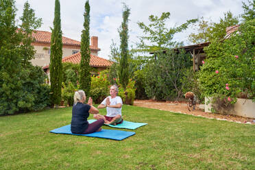 Serene senior couple meditating in summer villa garden grass - CAIF33796