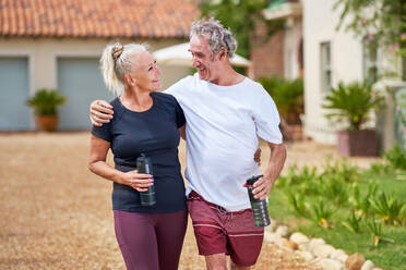 Happy, active senior couple hugging and walking outside villa - CAIF33801