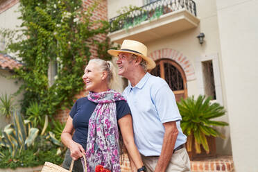 Happy senior couple looking away outside sunny villa - CAIF33804