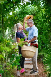 Happy senior couple with flowers under trellis in summer garden - CAIF33811