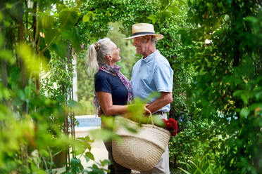 Happy senior couple hugging under lush green trellis in summer garden - CAIF33812