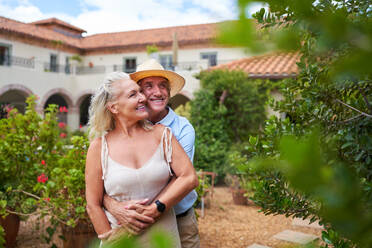 Happy senior couple hugging in garden outside summer villa - CAIF33817