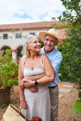 Portrait happy senior couple hugging outside summer villa - CAIF33818