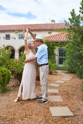 Happy senior couple dancing outside villa in summer garden - CAIF33820